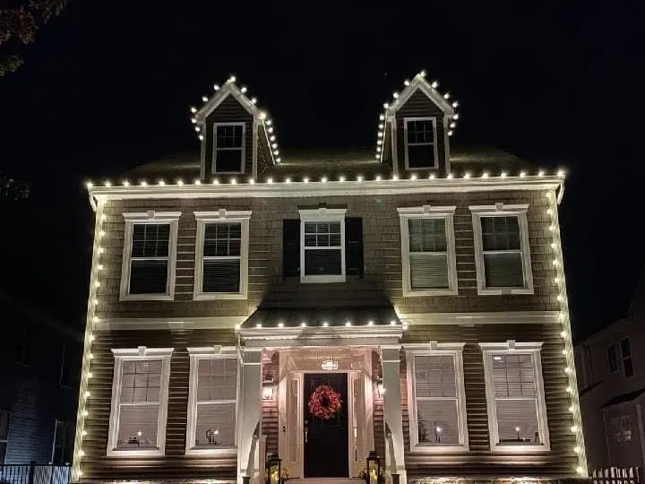 Two-storey home with its roofline, dormers and windows outlined in warm white Christmas lights at night