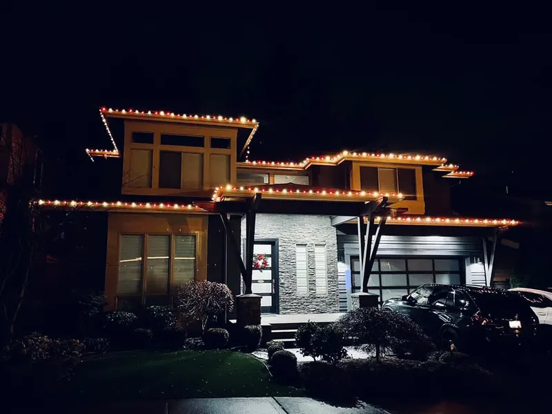 Modern two-storey home with flat rooflines traced in warm white lights at dusk