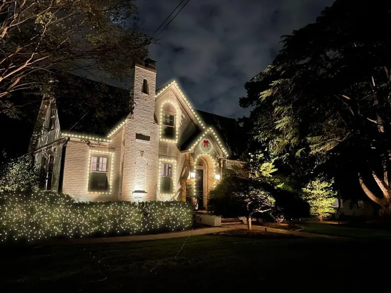 Tudor-style home with soft warm white lights on the gables and lit shrubs at night