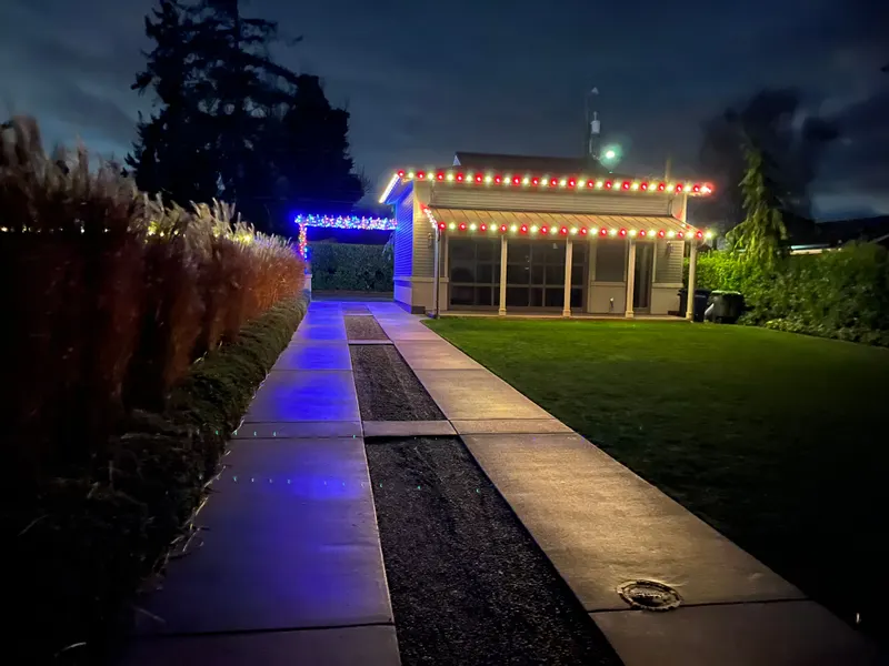 Home at dusk with red and warm white lights along the roofline, seen from the front walkway